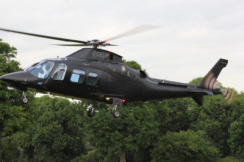 Agusta 109 helicopter flying low over trees on approach to land at Cheltenham