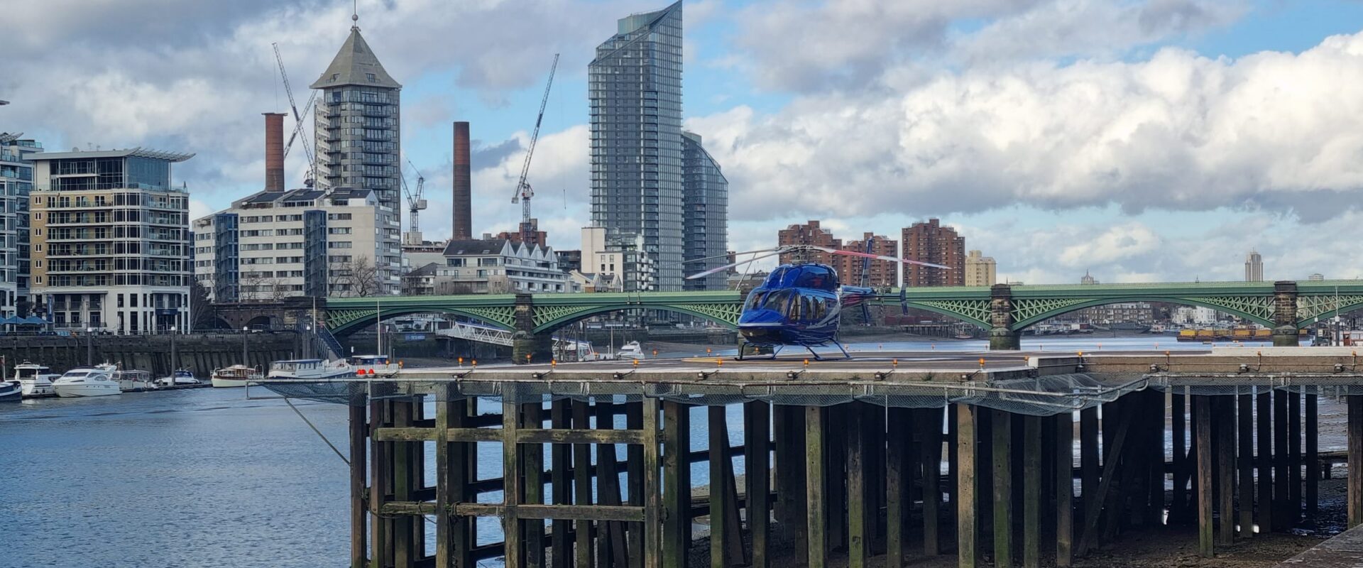 A helicopter on the river platform at Battersea Heliport, London, with the railway bridge and the River Thames behind it