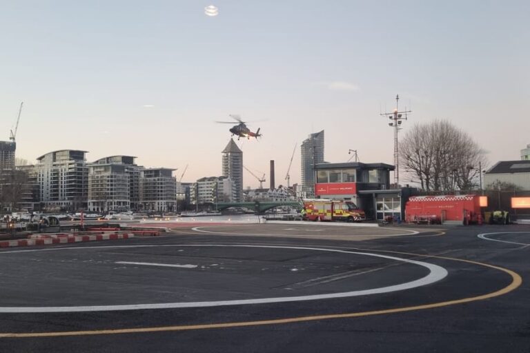 A helicopter arriving over the landing pad at London Heliport in Battersea at dusk, with the control tower and fire tender beside the Thames