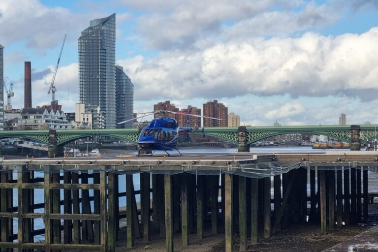 A helicopter on the river platform at London Heliport, Battersea, with the railway bridge and the Thames behind it
